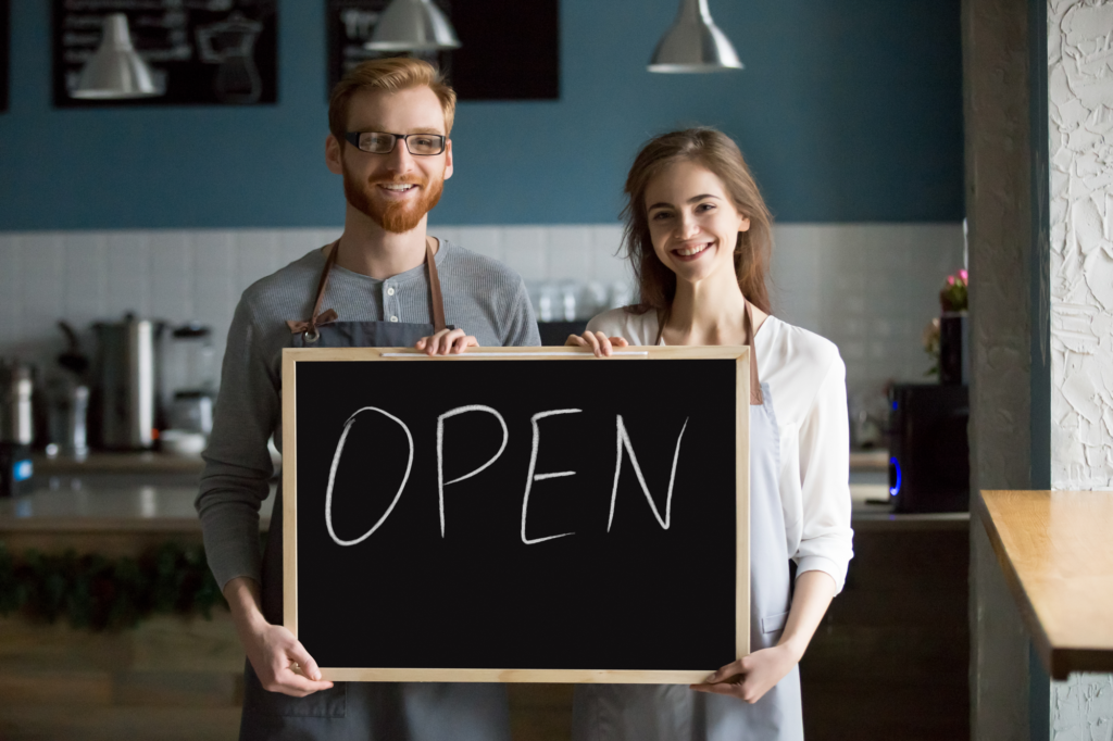 smiling-waiter-waitress-holding-chalkboard-with-open-sign-portrait مهاجرت به آلبرتا از طریق کارآفرینی در نواحی روستایی
